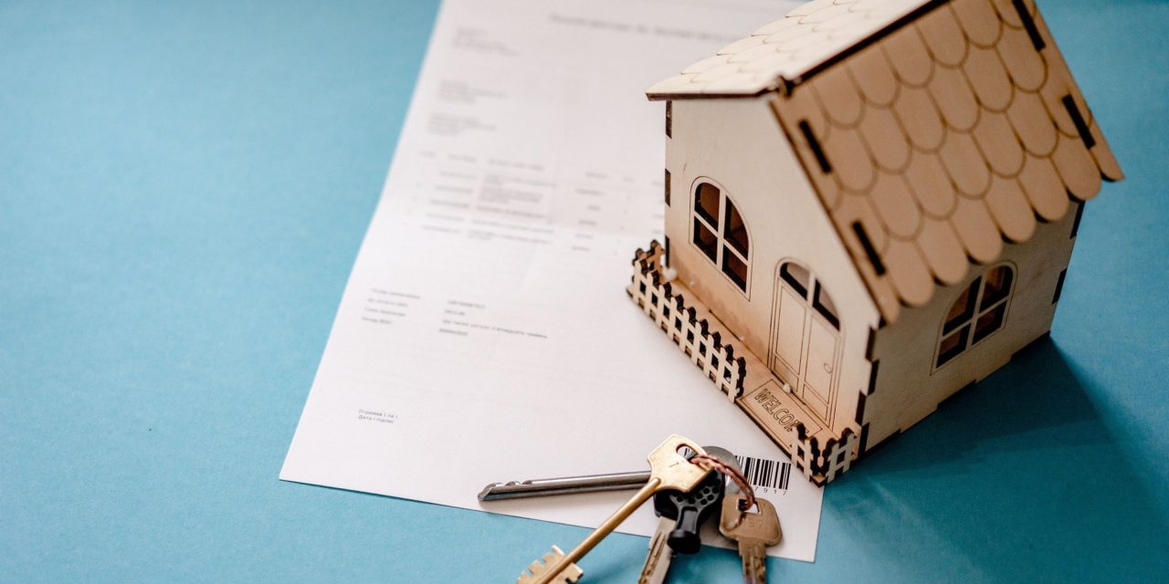 A mini house model and key set sitting on top of a real estate contract