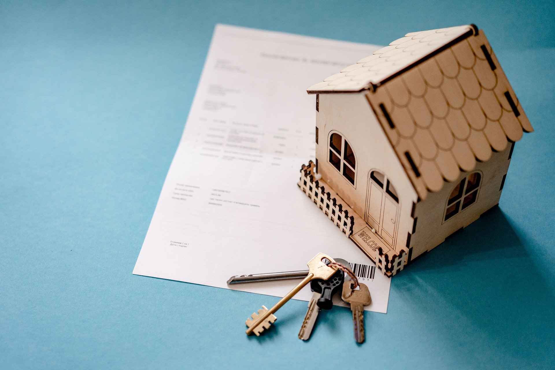 A mini house model and key set sitting on top of a real estate contract