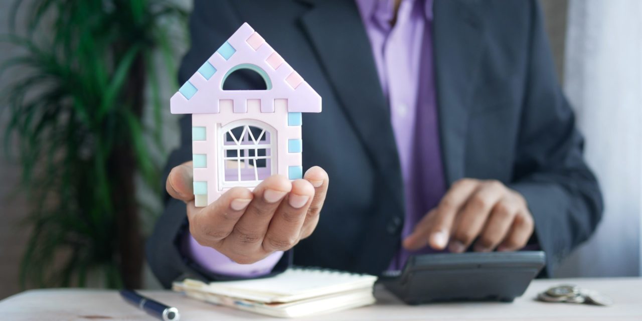 Professional holding decorative house and using a calculator